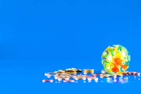 Virus knocking down a stack of different coins and money on a blue background with copy space. Covid-19 crisis concept. Economic crisis caused by coronavirus.の写真素材