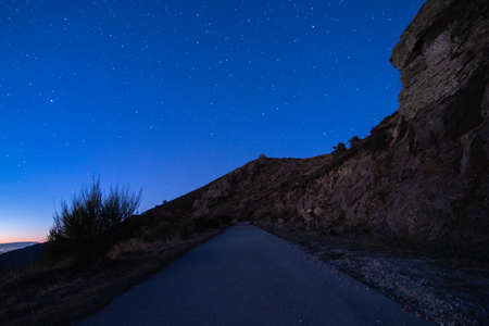 Countryside road with blue starry night sky in the mountain. Escaping in solitude into the wilderness. Connection to nature to the great outdoors.の写真素材