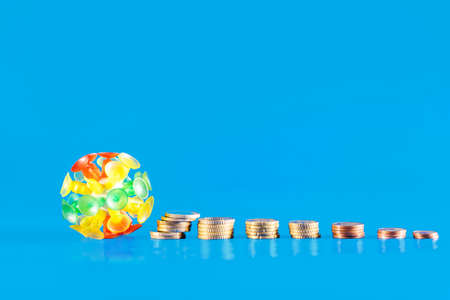 Covid-19 crisis concept. Virus knocking down a stack of different coins on a blue background. Covid 19 crisis money decreasing value. Economic crisis caused by coronavirus.の写真素材