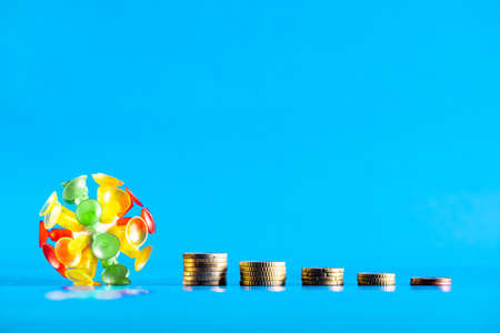 Isolated virus with different coins on a blue background. Covid-19 crisis money decreasing value. Economic crisis caused by coronavirus.の写真素材