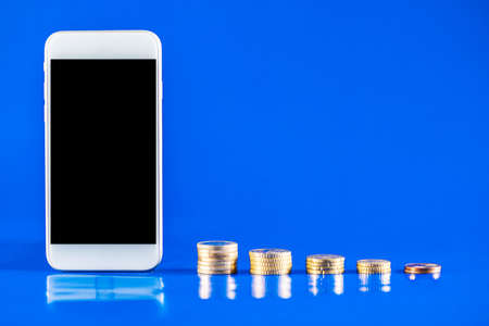 Mobile phone with stack of coins on blue background. Business growth and financial saving concept of...