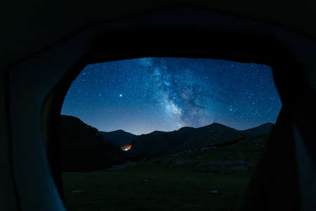 View of the Milky Way and mountains through the door of the tent. Camping in the mountains at night. Real outdoor adventure and wild life concept.の写真素材
