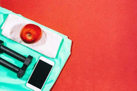 Attributes of a healthy lifestyle: apple, sport equipment, sports shirt, hand weights, mobile phone. Tools for fitness at home.の写真素材