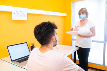 Teacher with a medical face mask teaching a student with a medical face mask at school.の写真素材