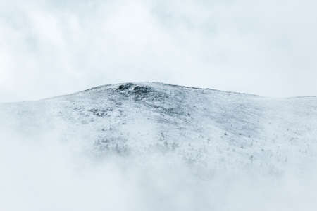 Snowy peak of a white mountain with fog and snow. Concept of cold and winter. Uncluttered white space.の写真素材