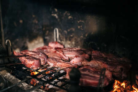Grilled meat in the fireplace of his home. Raw beef on a barbecue grill with the coals underneath.