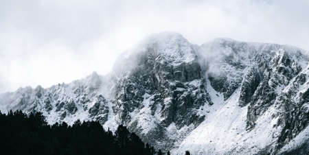 Winter landscape with snow-capped rocky mountains and the silhouette of pine trees. Snowy mountain range and mountain peaks. Mountainous landscape in winter with snow and fog.の写真素材
