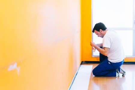 Painter man at work using painter's tape before paint the wall, room or business, isolated on big empty space with copy space.の写真素材
