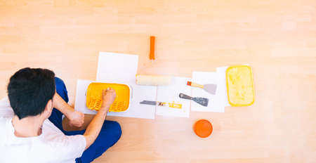 Painter man at work stirring and preparing a pot of orange paint with a paint brush to make reforms. Set of tools and utensils of a painter, top view. Occupation of painter, banner, anonymous person.の写真素材