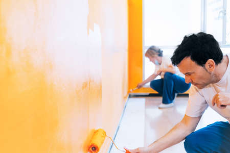 Man and woman painting a wall orange with the roller. Staff of painters doing renovations and reforms as a team.の写真素材