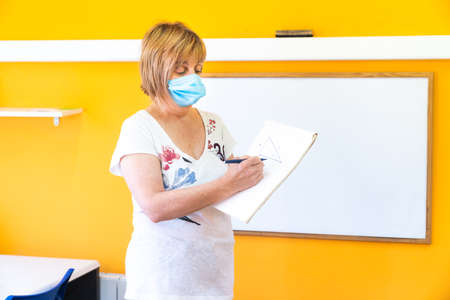 Teacher with medical face mask doing class at school in the new normal. Going back to school after coronavirus pandemic with the necessary preventive measures.の写真素材