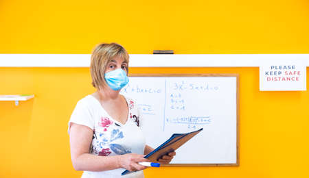 Teacher at a school academy giving classes in a summer school wearing a medical face mask and respecting social distance measures in the new normal.の写真素材