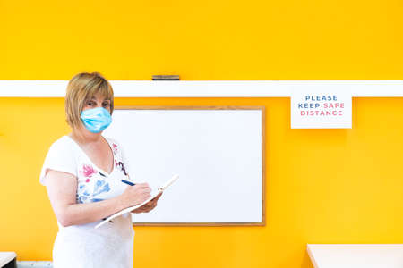 Teacher with medical face mask doing class at school in the new normal. Teaching during the coronavirus pandemic with the necessary preventive measures. Going back to school.の写真素材
