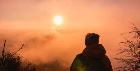 Young traveler man observing the sun on a beautiful sunset or sunrise. Rear view of adventurer backpacker. Concept of traveling, freedom and adventure.の写真素材