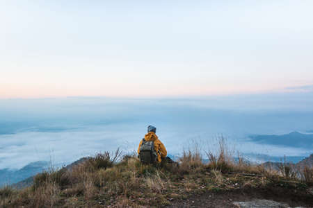 Young traveler backpacker sitting in the top of the mountain observing the landscape covered by a...
