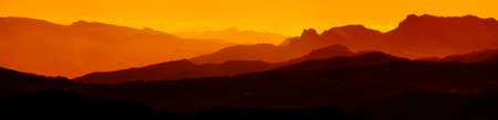 Extra wide panorama of mountain landscape at down. Majestic sunset or sunrise colors over the mountains. Dramatic scene. Beauty world.の写真素材