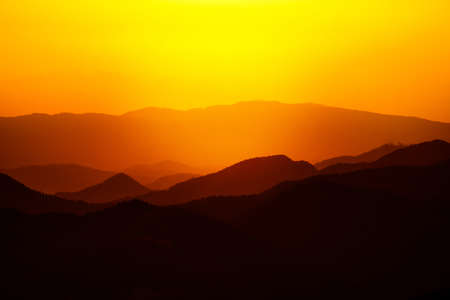 Beautiful sunset or sunrise colors over the mountains. Majestic colorful landscape in the mountains. Dramatic dark orange and red mountain landscape with fog.の写真素材