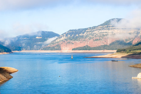 Landscape of the Sau swamp with its church. Tourism in Sau Reservoir, Osona, Barcelona, Catalunya, Spain. Colorful scene of a sunny day from a swamp with blue water in a mountainous landscape.の写真素材