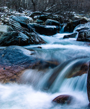 Mountain river frozen in winter with very cold blue water. The water flows down a mountain stream....