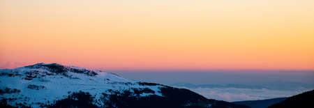 Panoramic view of snowy mountains ranges at sunrise or sunset. Calm and relaxing nature mountainous natural scenery. Nature background landscape with orange and warm colors in the mountains at dusk.の写真素材