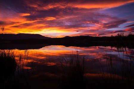 Spectacular sunset with orange and red clouds reflected in the lake water. Natural mirror at sunrise. Estany de Banyoles, Girona, Catalonia, Spain.の写真素材