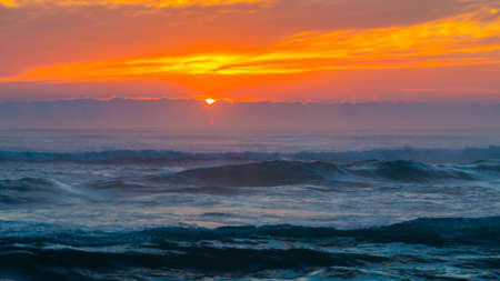 Sunrise at sea. The sun rises over the horizon of the sea and a new day begins. Panoramic sea landscape on sunset or sunrise with ocean waves and orange colorful clouds in sky.の写真素材