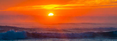Sunrise at sea. The sun rises over the horizon of the sea and a new day begins. Panoramic sea landscape on sunset or sunrise with ocean waves and orange colorful clouds in sky.の写真素材