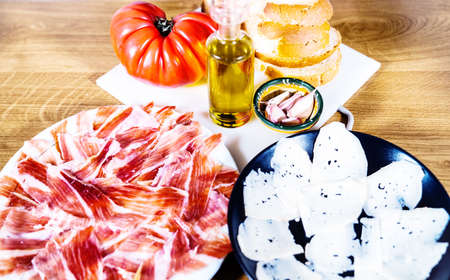 Typical Catalan or Spanish food. Bread with tomato, Iberian ham plate, goat cheese, olive oil and garlic. Traditional food and food products on a wooden background.の写真素材