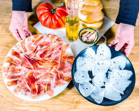 Plate of Iberian ham and goat cheese served in two plates on a wooden background. Typical spanish or catalan food: serrano ham, cheese bread with tomato, red wine, oil and garlic.の写真素材