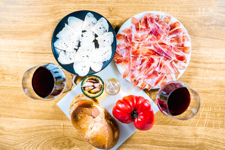 Typical Catalan or Spanish food. Bread with tomato, Iberian ham, glass of black wine, goat cheese,...