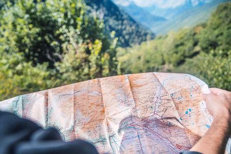 Anonymous person looking the travel route on a map in the mountain. Routes, excursions and mountain trails through nature in summer. Concept of exploring and live adventures traveling in nature.の写真素材