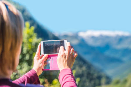 Woman taking a photo with the mobile to a mountainous landscape. Routes, excursions and mountain summer trails through nature in family. Concept of exploring and live adventures traveling in nature.の写真素材