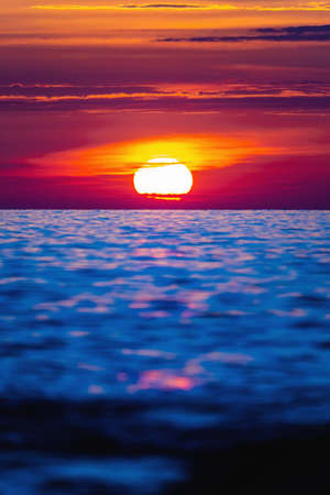 Colorful sunset with large bright sun under the sea surface. Sea sunset, ocean sunrise, seascape.の写真素材
