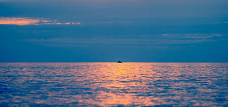 Fishing boat in the middle of the sea at sunrise or sunset. Panorama view of lone fisherman going out to fish in the ocean in the morning. Vacation, relaxation, tranquility and loneliness concept.の写真素材
