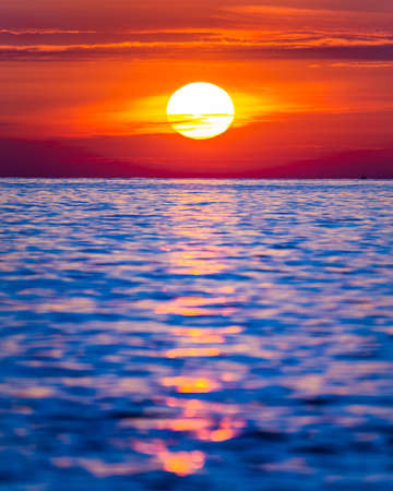 Bright sunset with large yellow sun under the sea surface.の写真素材
