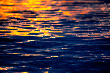 Sea waves texture with sunset or sunrise light reflecting on the water. Sunbeams illuminate on the blue ocean water with warm orange sunlight. Artistic and creative nature background.の写真素材