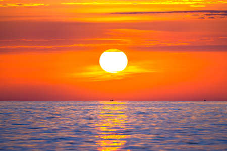 Sun rising in the sea with a fishing boat in the rays of the sun above the waves. Beautiful sunrise on the ocean with a big and colorful sun in summer. A new day begins.の写真素材