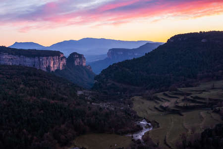 Landscape of a valley with towering rocky mountains with a beautiful sky with pink and orange clouds at sunset. Cingles de Tavertet, Collsacabra, Osona, Barcelona, Catalonia, Spain.の写真素材