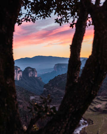 Landscape of a valley with towering rocky mountains with a beautiful sky with pink and orange clouds at sunset. Cingles de Tavertet, Collsacabra, Osona, Barcelona, Catalonia, Spain.の写真素材