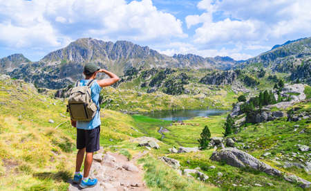 Young traveler man with a backpacker standing on an alpine mountain trail with a lake. Circo de Saboredo, Aran Valley, Catalan Pyrenees, Catalonia, Spain, Europe.の写真素材