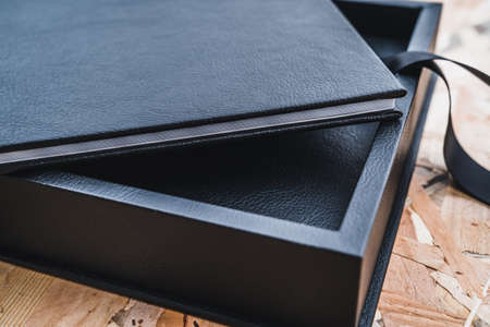 Black leather photo album on a table with vintage wood background. Wedding or family photo book...