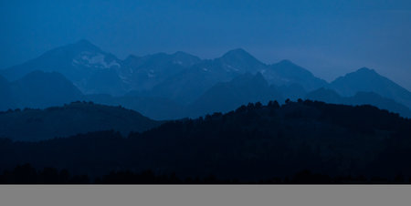 Panoramic mountains layers during blue hour. Landscape with dark blue misty silhouettes of alpine mountains and fir trees forest in Pyrenees.の写真素材