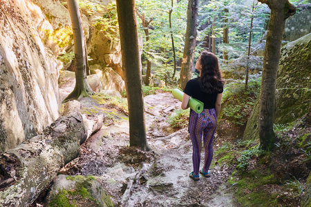 Young attractive girl standing in sun light in mountain forest. Preparing for practicing yoga on a yoga mat.の写真素材