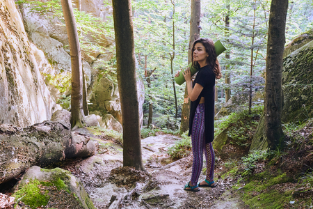 Young attractive girl standing in sun light in mountain forest. Preparing for practicing yoga on a yoga mat.の写真素材