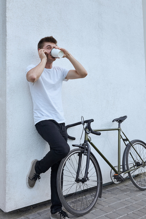 Young hipster style man posing with bicycle on the street sport style picture handsome guy white wallの写真素材
