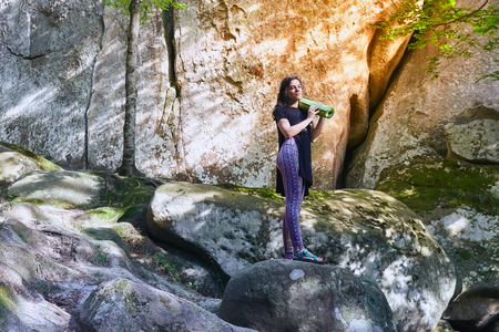 Young attractive girl standing on the big rock in mountain. Preparing for practicing yoga on a yoga mat.の写真素材