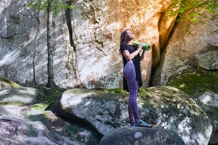 Young attractive girl standing on the big rock in mountain. Preparing for practicing yoga on a yoga mat.の写真素材