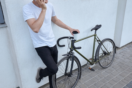 Young hipster style man posing with bicycle on the street sport style picture handsome guy white wallの写真素材