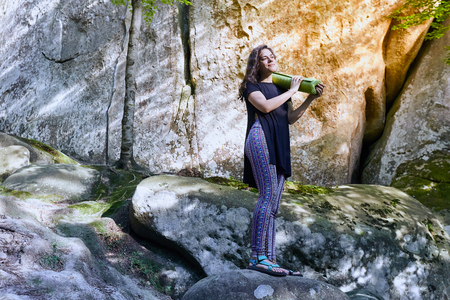 Young attractive girl standing on the big rock in mountain. Preparing for practicing yoga on a yoga mat.の写真素材
