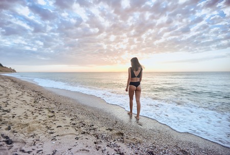 Brunette tanned girl in swimwear enjoying and walking on beach